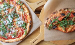 Freshly baked pizzas topped with prosciutto, arugula, and cheese, served on wooden boards. - Photo by Valeria Boltneva on Pexels